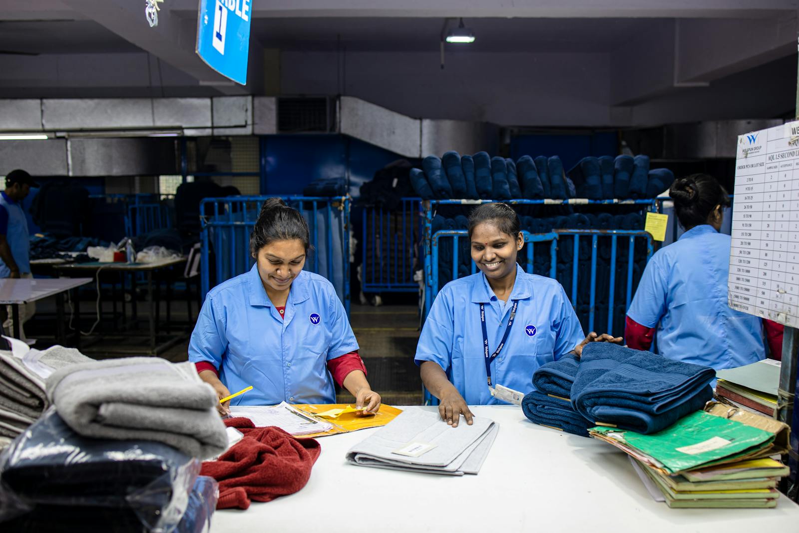 Two female textile workers sorting fabrics in a factory setting, wearing blue uniforms.